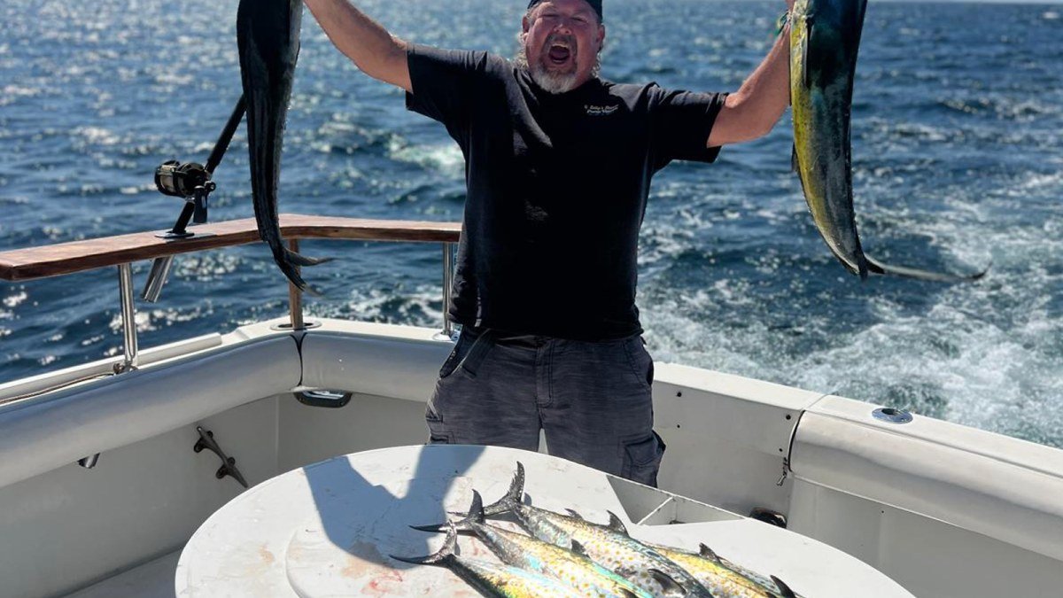 An angler holding two dorado in the cockpit of the 54 ft Hatteras sportfishing charter out of Nuevo Vallarta