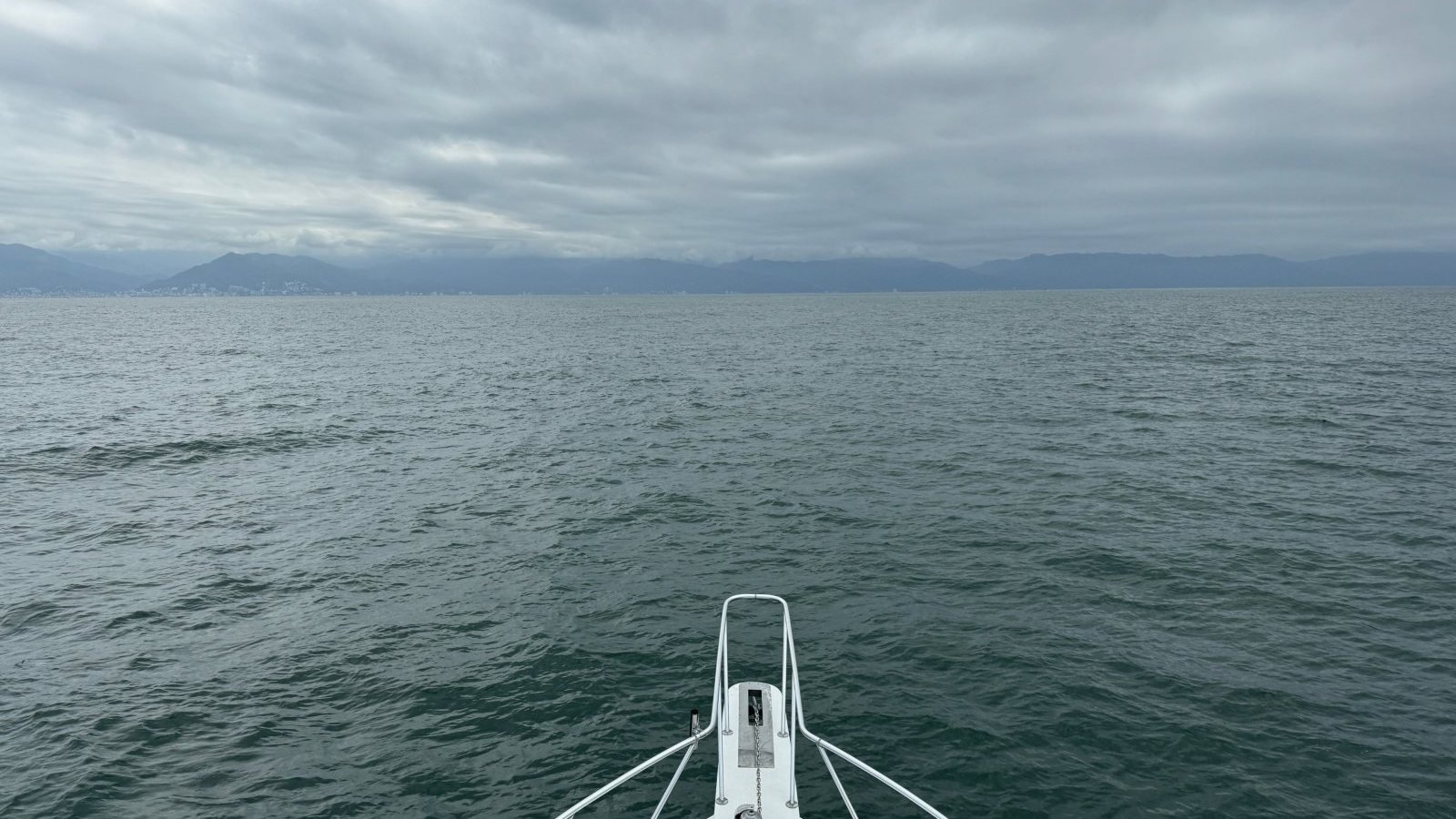 View from the bow of a fishing boat heading out across a calm, overcast Banderas Bay early in the morning