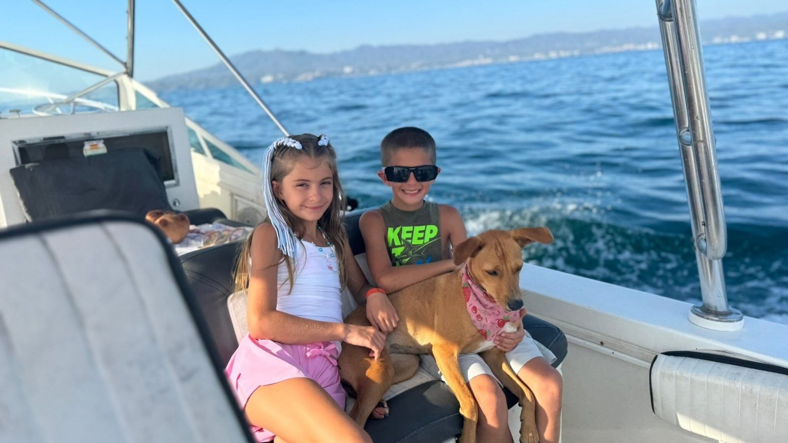 Two children sitting with the boat dog under the shade canopy of a family fishing charter in Banderas Bay