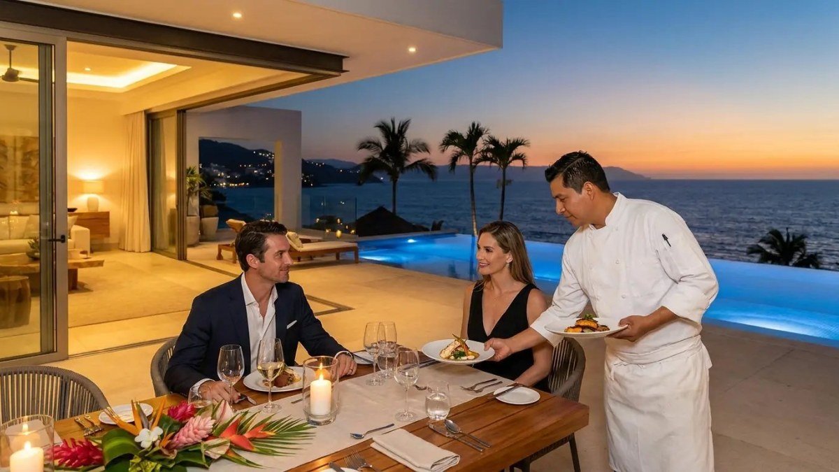 A PVR Private Chef serving a plated course to a couple at their villa dining table as the sun sets over the bay