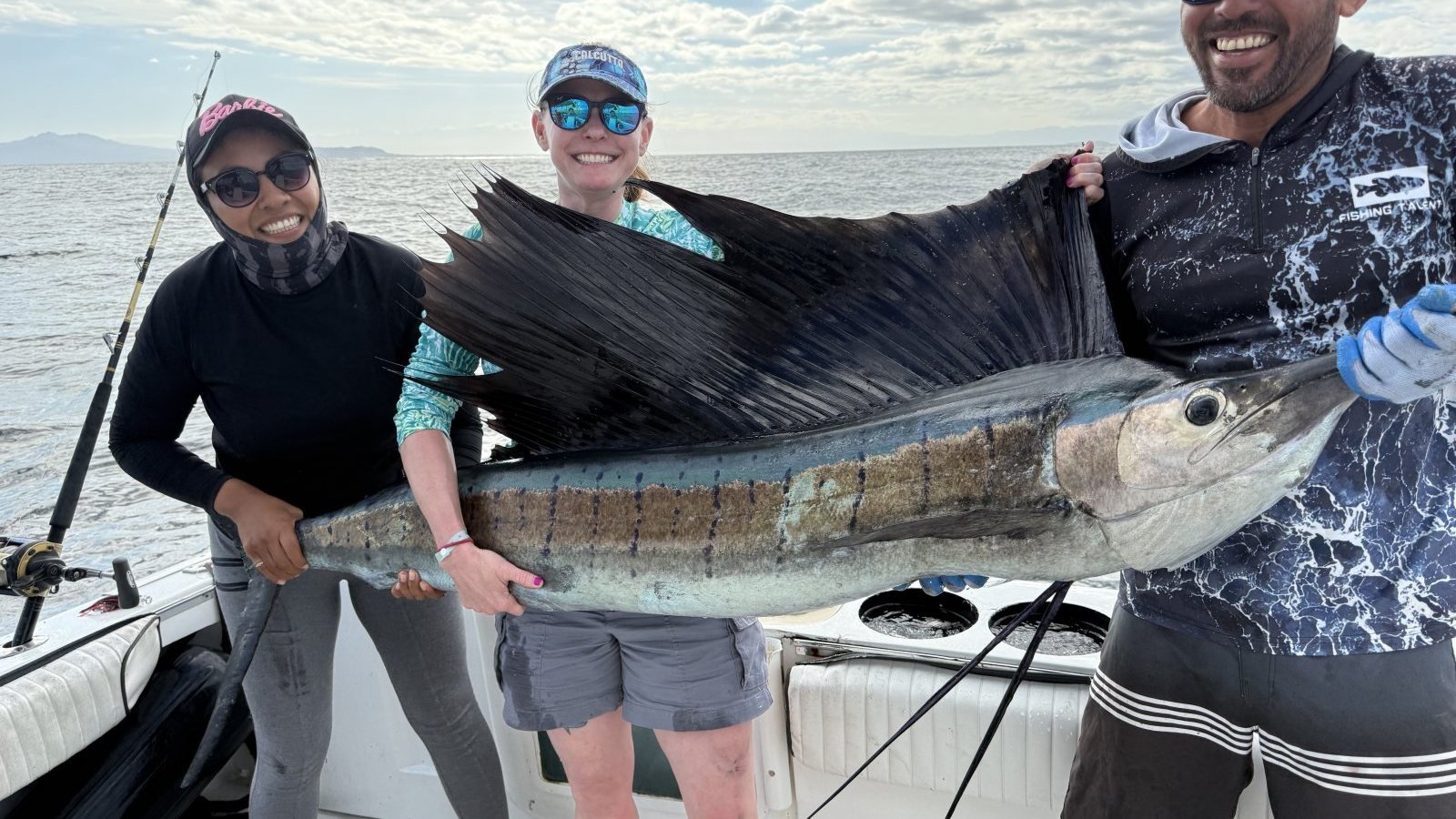 Three anglers holding a large sailfish across the stern of a charter boat in Banderas Bay, Puerto Vallarta