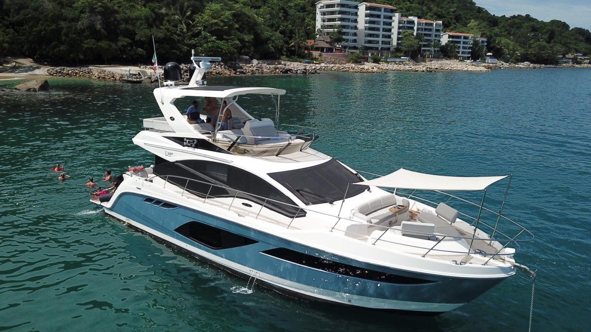 A crewed motor yacht anchored below the green cliffs south of Puerto Vallarta on a private charter in Banderas Bay